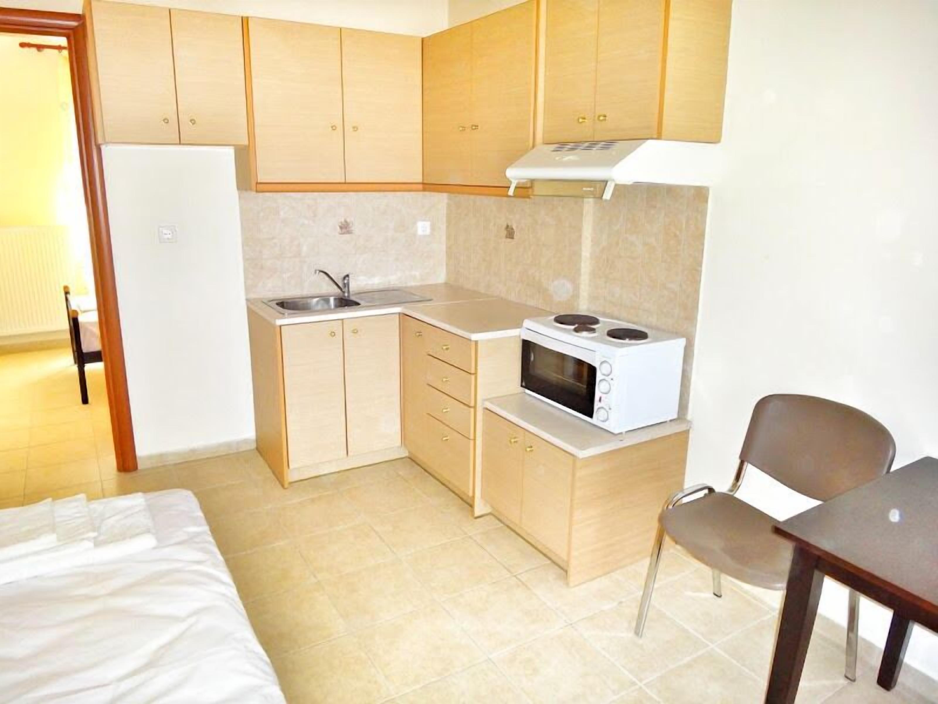 Una cocina compacta con armarios de madera, un microondas, un lavamanos y una zona de comedor con una silla y una mesa.