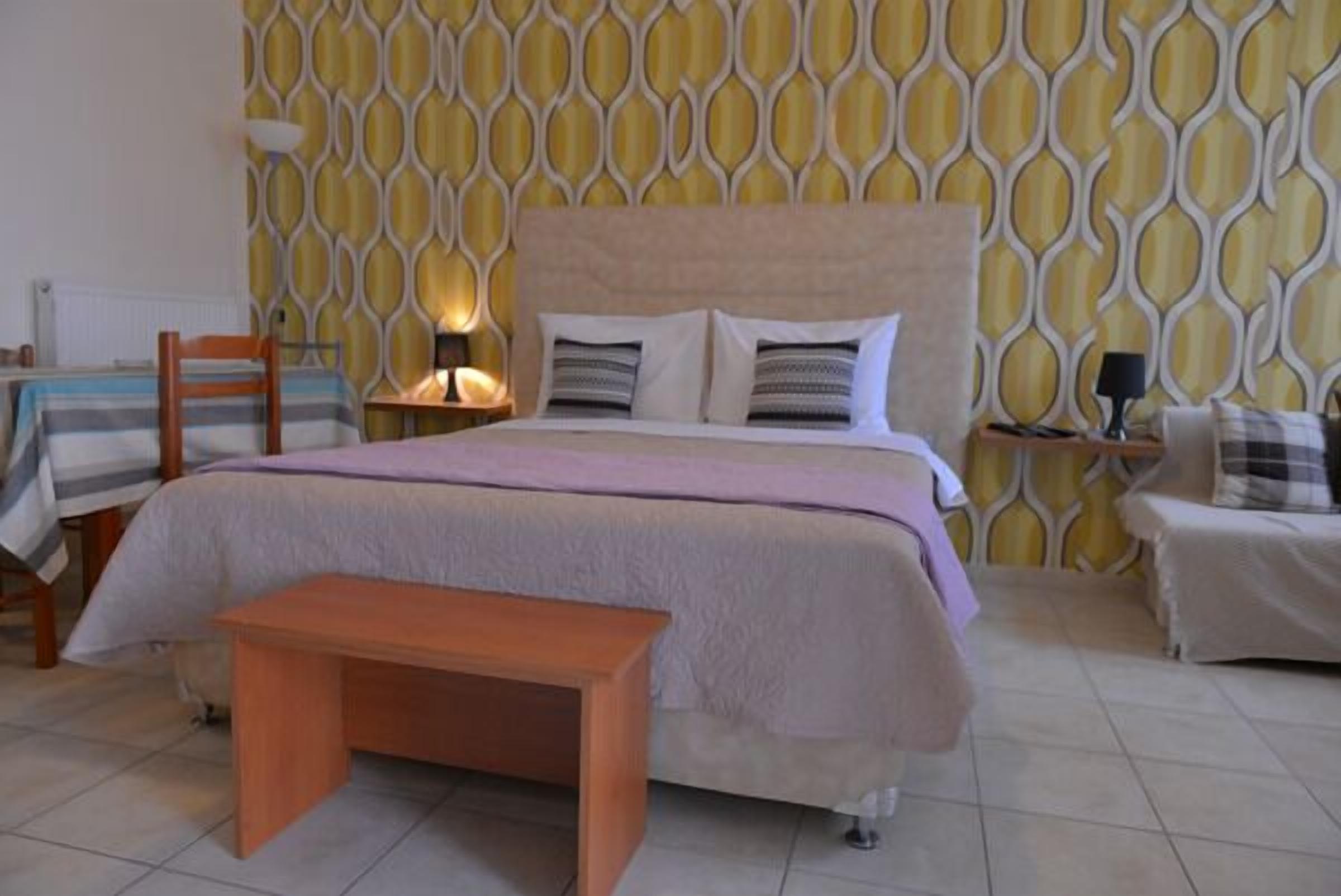 A bedroom with a bed, bedside tables, a bench, and a patterned wall.