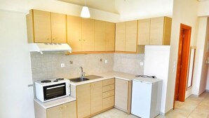 Una cocina compacta con armarios de madera clara, una estufa blanca, un fregadero y un refrigerador pequeño.