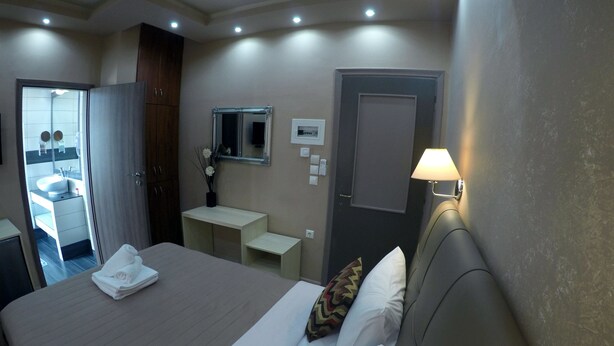 Habitación de hotel con cama, mesita de noche, lámpara, espejo y baño visible a través de una puerta abierta.