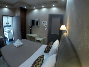 A hotel room with a bed, bedside table, lamp, mirror, and a bathroom visible through an open door. - Midia Suites (Livadia)