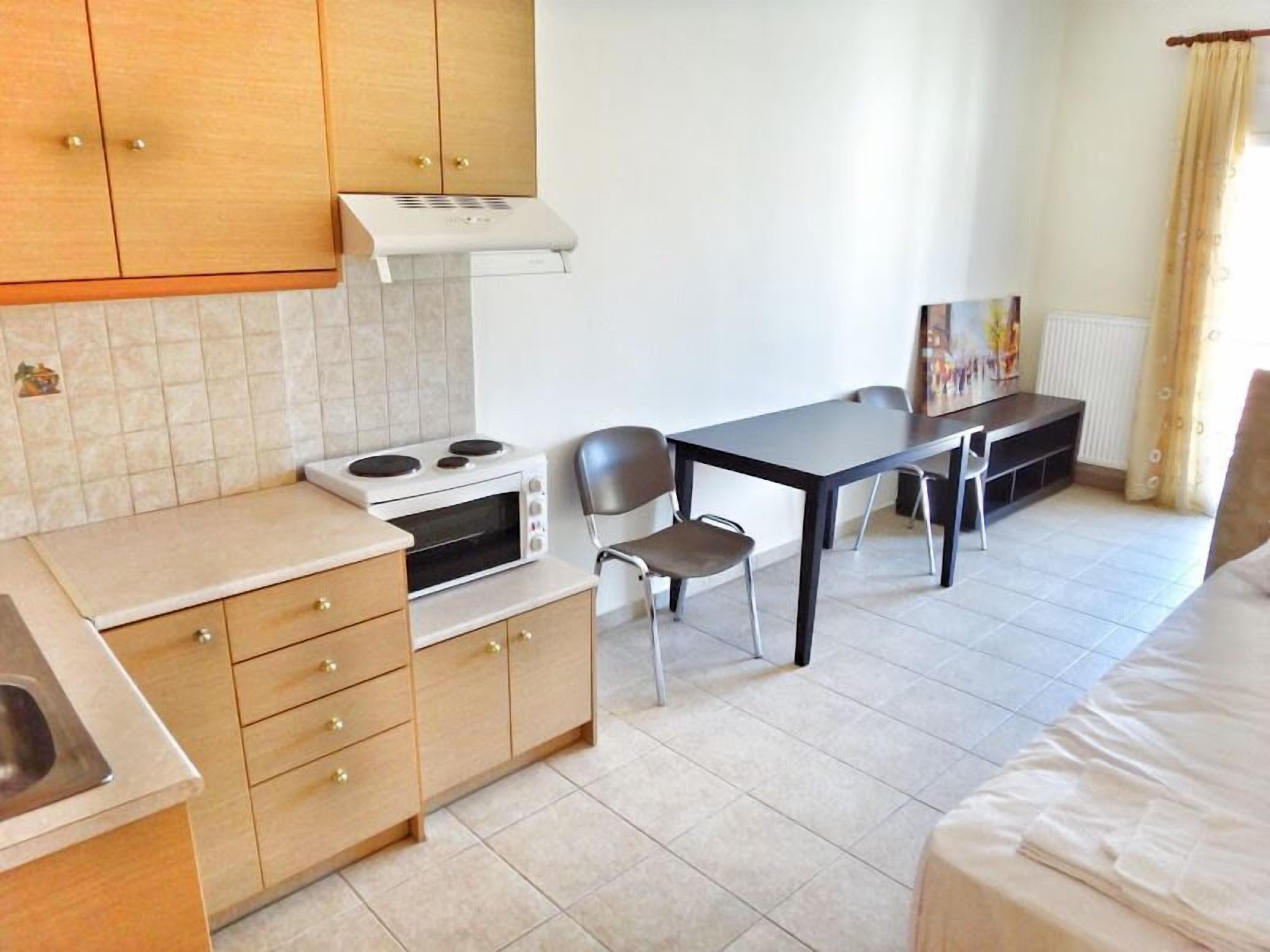 Une cuisine compacte équipée d’une cuisinière, d’un four à micro-ondes et de meubles de rangement en bois. La pièce comprend également une table à manger avec des chaises et un lit.