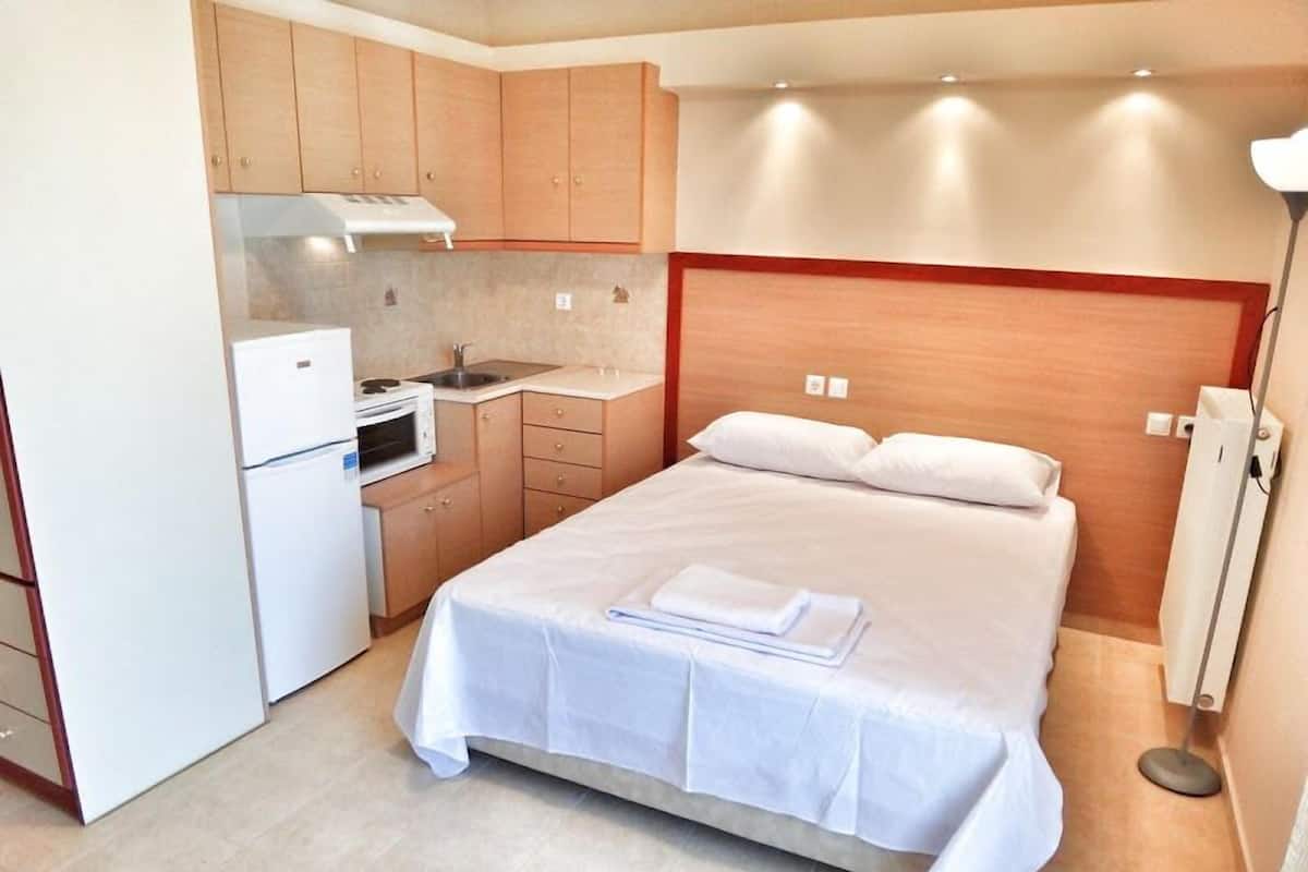 A compact hotel room with a single bed, a kitchenette, and a small bathroom.