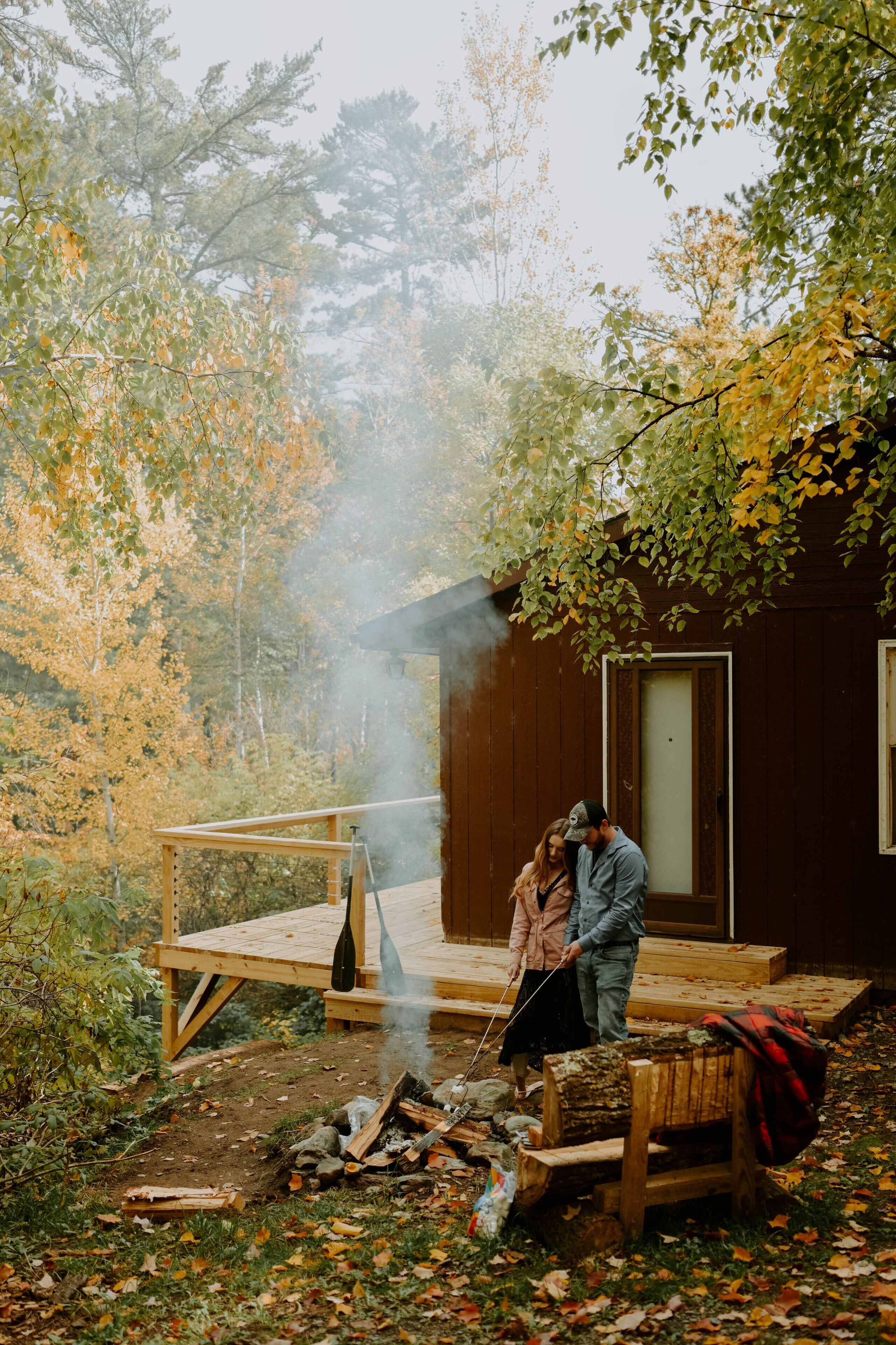 A rustic cabin with a wooden deck, a fireplace, and a bench.