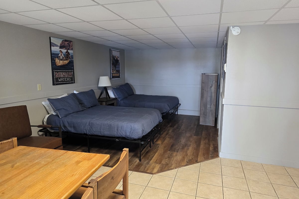 Habitación de hotel con dos camas, una mesa de madera, una silla y piso de baldosas.