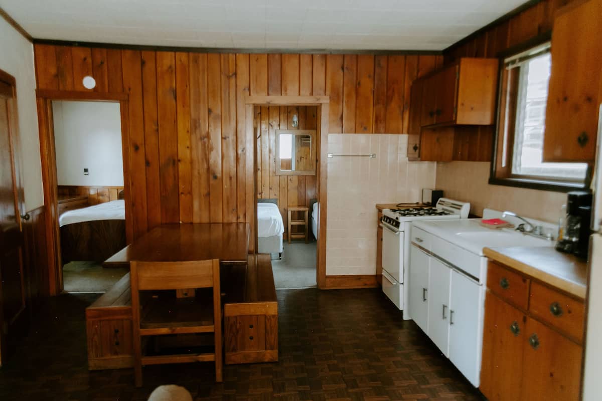 Cocina con paneles de madera, una mesa de comedor, armarios blancos y un refrigerador.