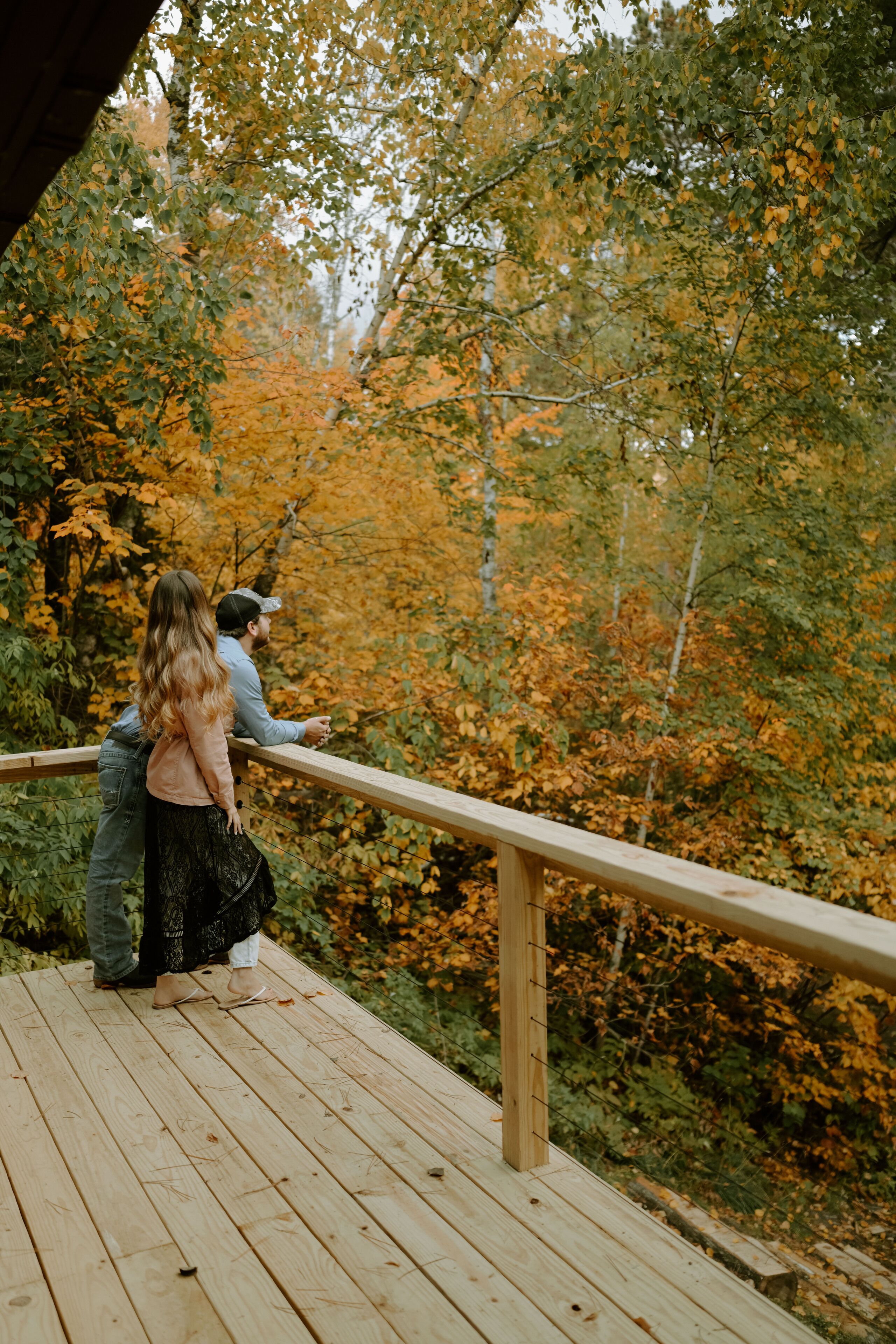 A wooden deck with a railing overlooking a forested area with autumn foliage.