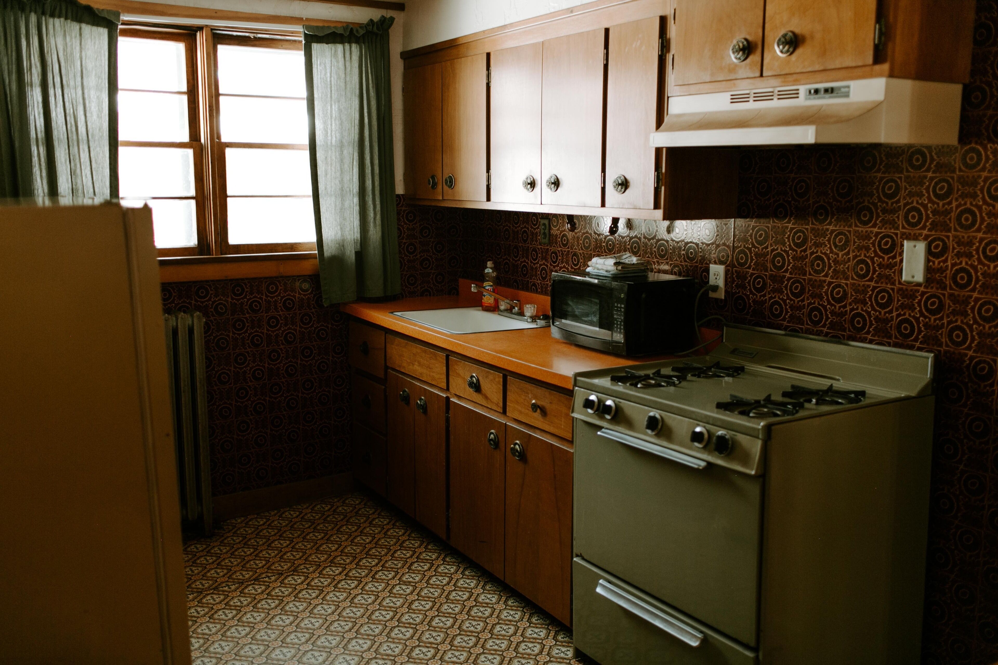 A kitchen with wooden cabinets, a stove, a microwave, and patterned tiles.