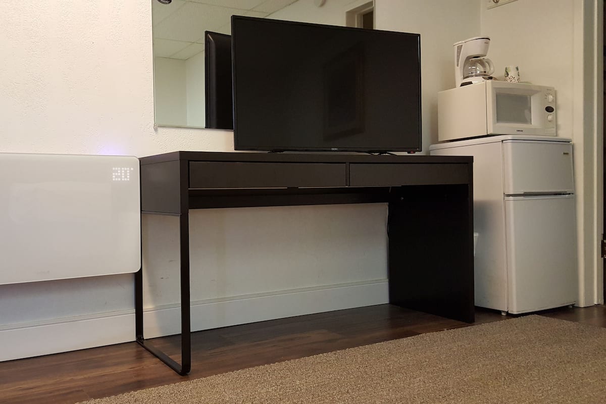 A compact kitchenette with a microwave, a small refrigerator, and a flat-screen TV mounted on a black desk.