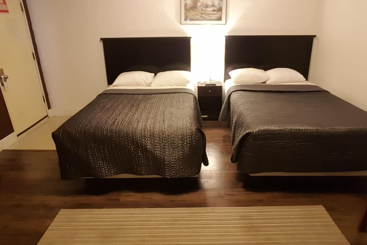A room with two beds, a wooden floor, a painting on the wall, and a door on the left.