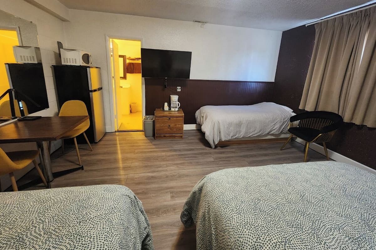 A hotel room with two beds, a desk, a chair, a TV, and a small table with a coffee maker.