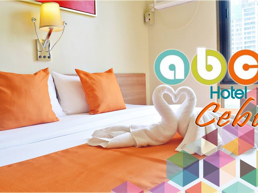 A hotel room with a bed, orange pillows, a white towel, and a lamp.
