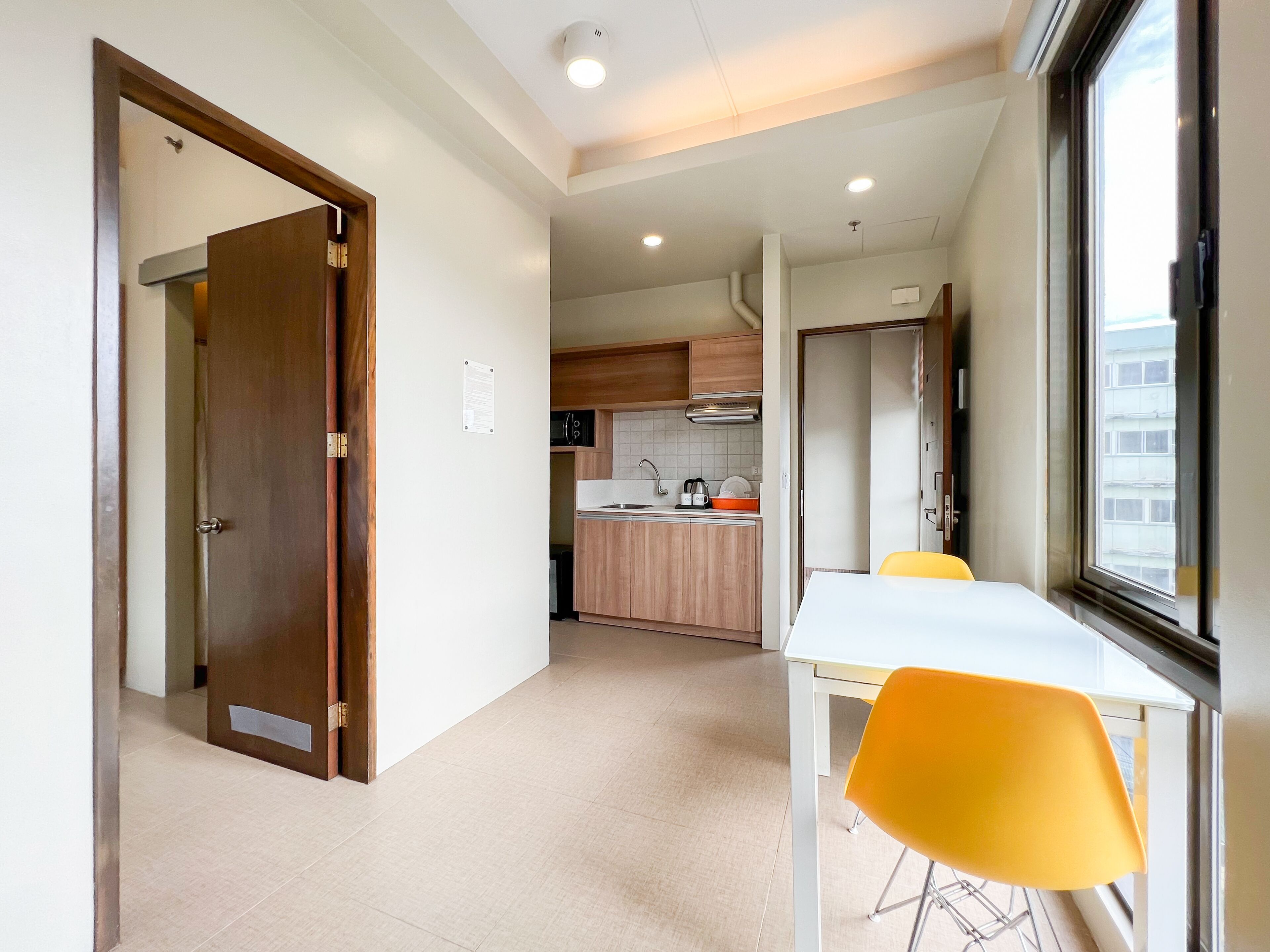 A modern kitchen with wooden cabinets, a white countertop, and a built-in oven. There is a dining area with a white table and yellow chairs.