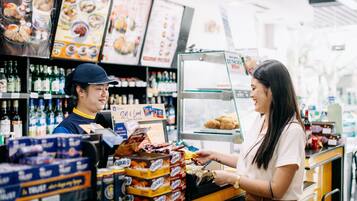 Una persona frente a un mostrador en una tienda, posiblemente una panadería o charcutería, con diversos alimentos y condimentos a la vista.