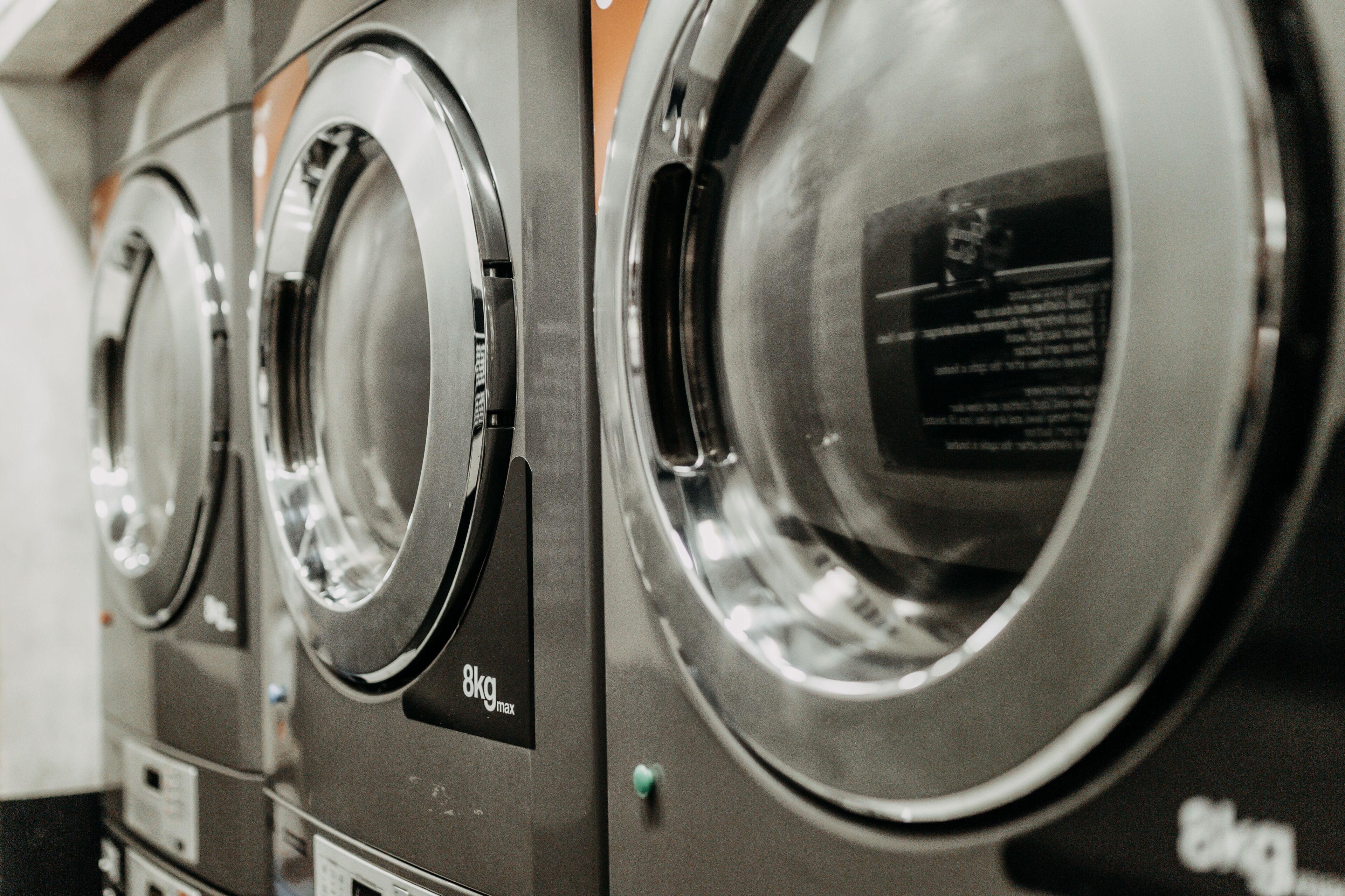 A row of front-loading washing machines with a label indicating a maximum load capacity of 8kg.