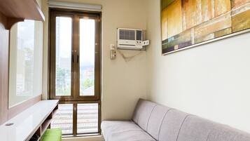 A living room with a grey sofa, a wooden TV stand, a green cushion, a ceiling light, and a colorful abstract painting.