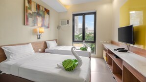 Habitación de hotel con dos camas, un televisor de pantalla plana, un escritorio y una ventana con vistas a edificios.