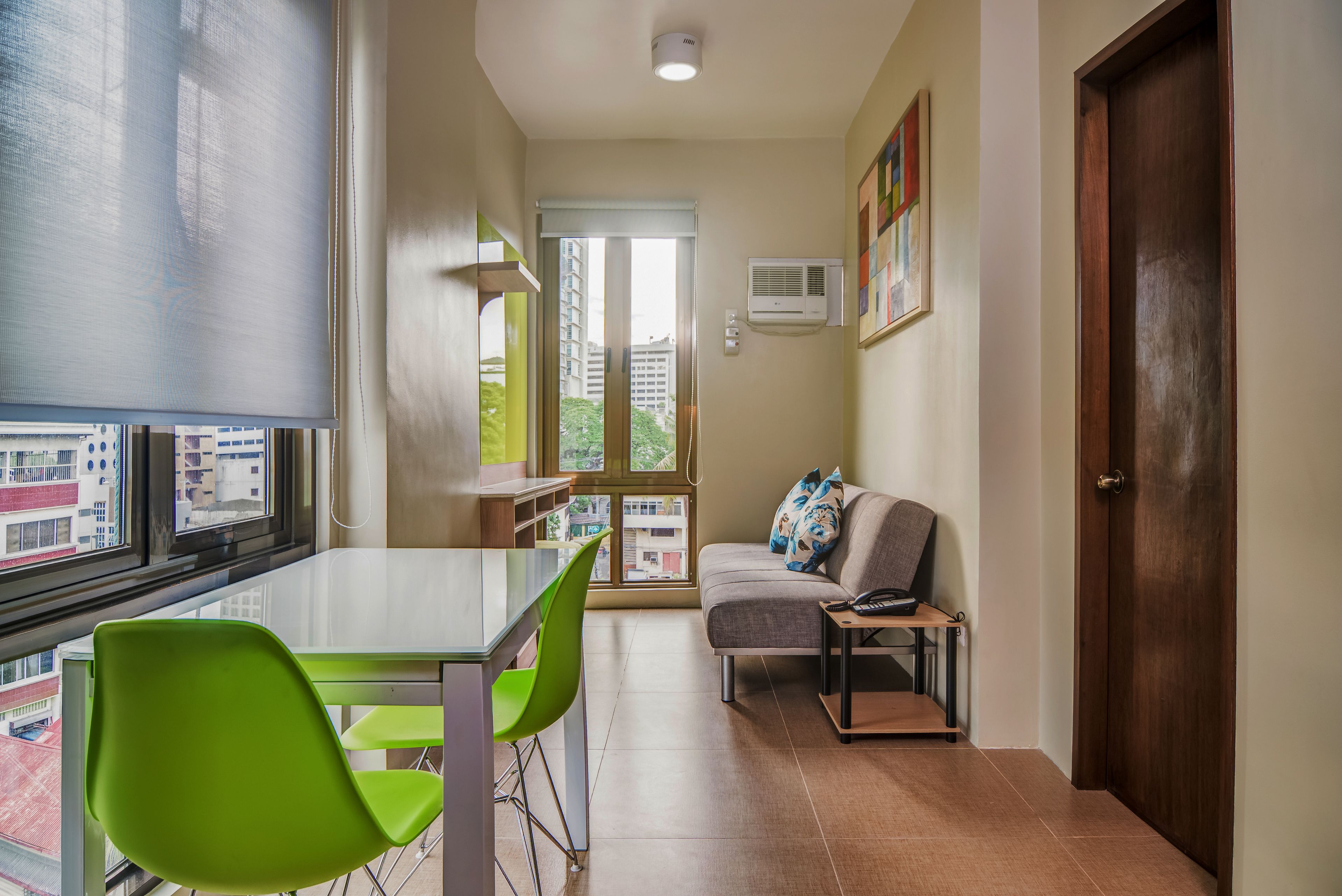 A modern living room with a glass table, green chairs, a grey sofa, and a wooden door.