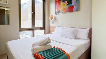 A hotel room with a large bed, a window with a view, a painting on the wall, and a lamp.