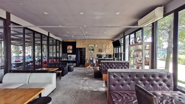 A modern cafe with leather seating, large windows, and a coffee bar in the background. - De Coco House (Si Racha)