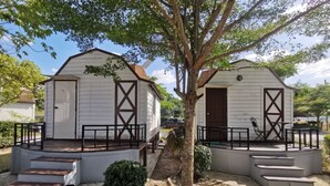 Two white cabins with wooden decks and black railings, surrounded by trees and a clear sky. - De Coco House (Si Racha)