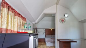 A compact hotel room with a kitchenette, a bed, a small dining area, and a bathroom visible through an open door. - De Coco House (Si Racha)