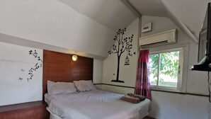 A bedroom with a wooden headboard, a bed with pillows, a nightstand, a wall-mounted air conditioner, a window with curtains, and a wall decoration of a tree with birds. - De Coco House (Si Racha)