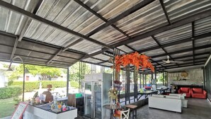 An outdoor covered area with a bar, seating, and a refrigerator. - De Coco House (Si Racha)