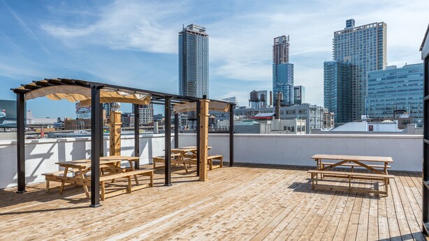 Une terrasse sur le toit, dotée de tables de pique-nique en bois et d’une pergola, offrant une vue panoramique sur les gratte-ciel de la ville.