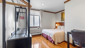 Une chambre d’hôtel avec un lit, un bureau, une chaise, une fenêtre avec des stores, un tableau au mur et un panneau « Il est interdit de fumer ».