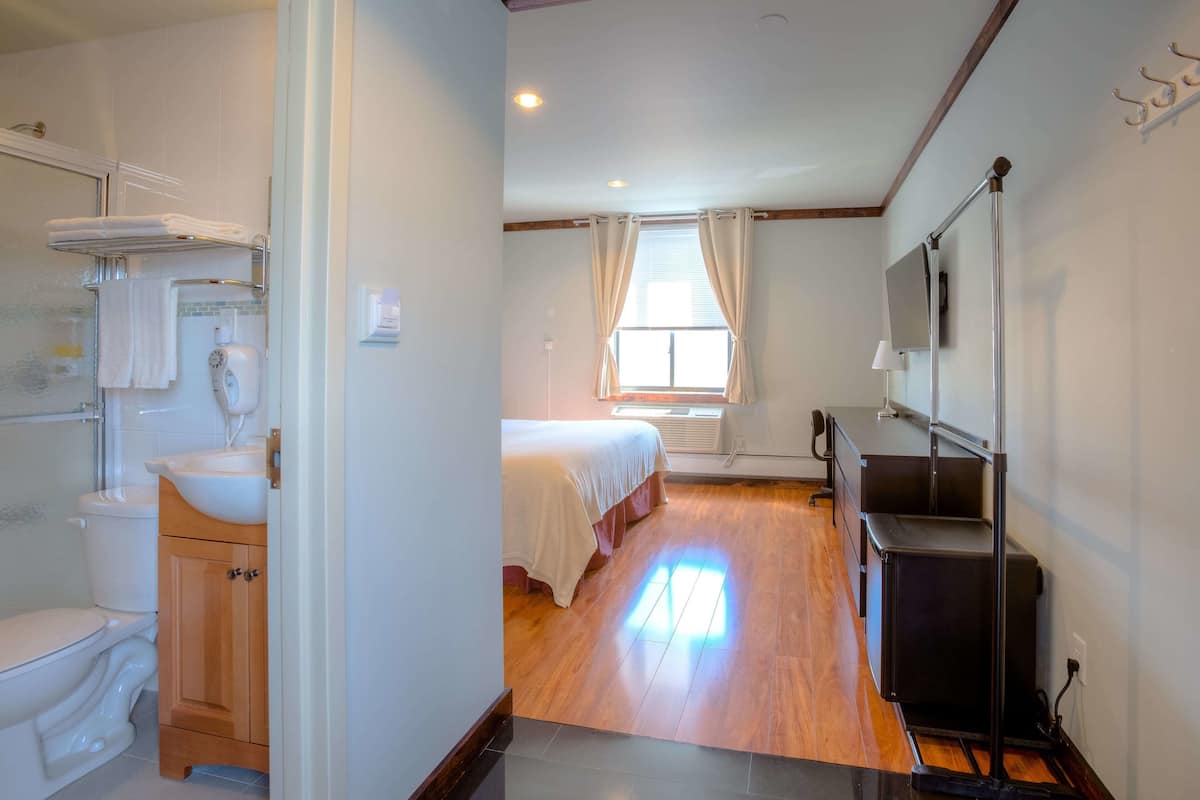 A hotel room with a wooden floor, a bed, a bathroom with a toilet and sink, and a TV mounted on the wall.