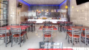 Restaurante com balcão central, várias mesas e cadeiras, e design de interiores moderno.