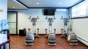 Une salle de sport équipée de trois vélos d’appartement, d’un distributeur d’eau et d’un téléviseur fixé au mur.