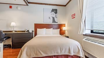 Une chambre d’hôtel comprenant un lit, des tables de chevet, un bureau, une chaise, une lampe, un tableau ou une œuvre d’art mural, une fenêtre avec des stores et un panneau « interdiction de fumer ».