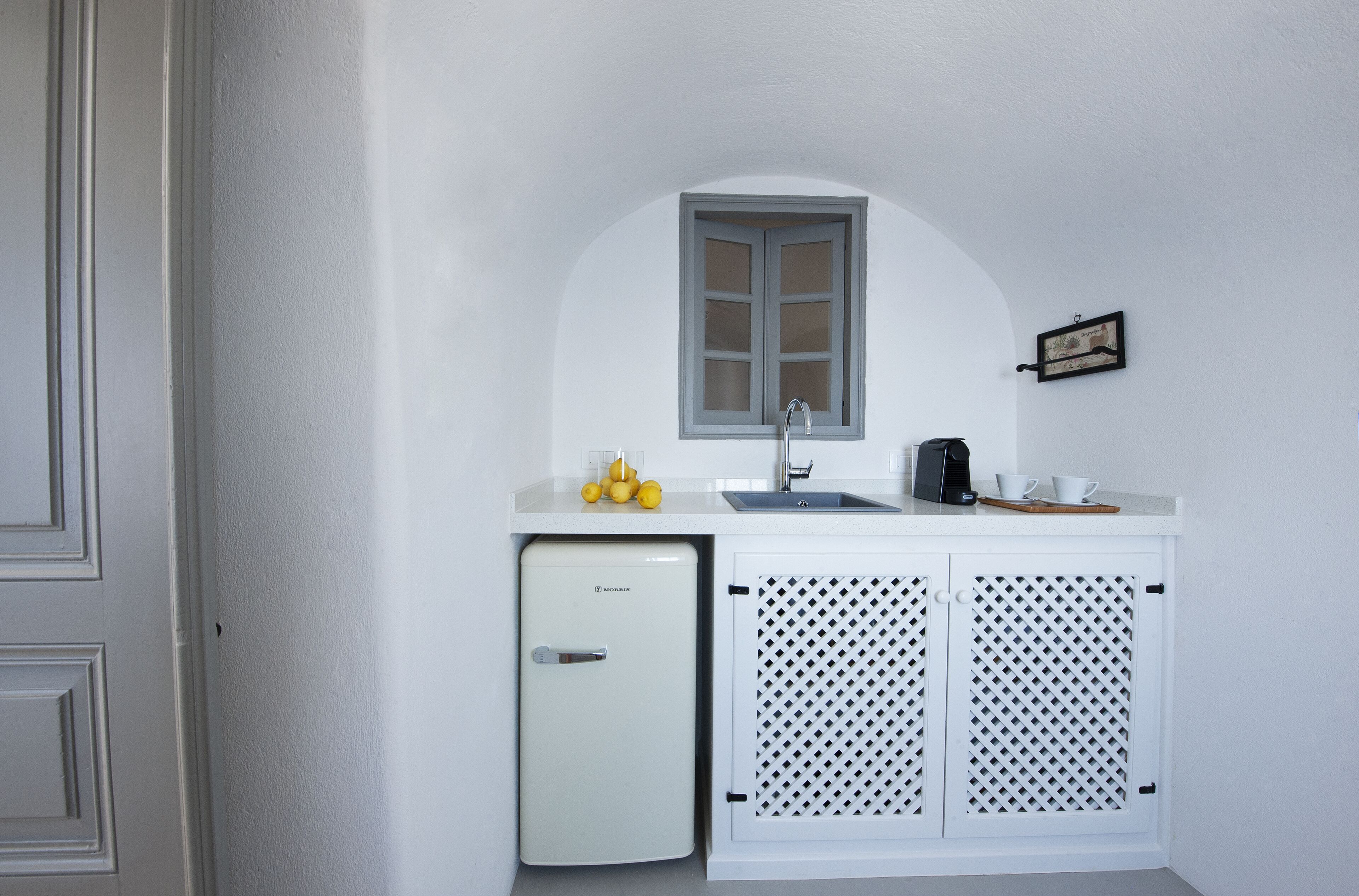 A compact kitchenette with a small refrigerator, a sink, and a window above it.