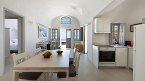 A spacious kitchen with a dining area, white cabinetry, and a large window. - Ikia Kriton (Santorini)