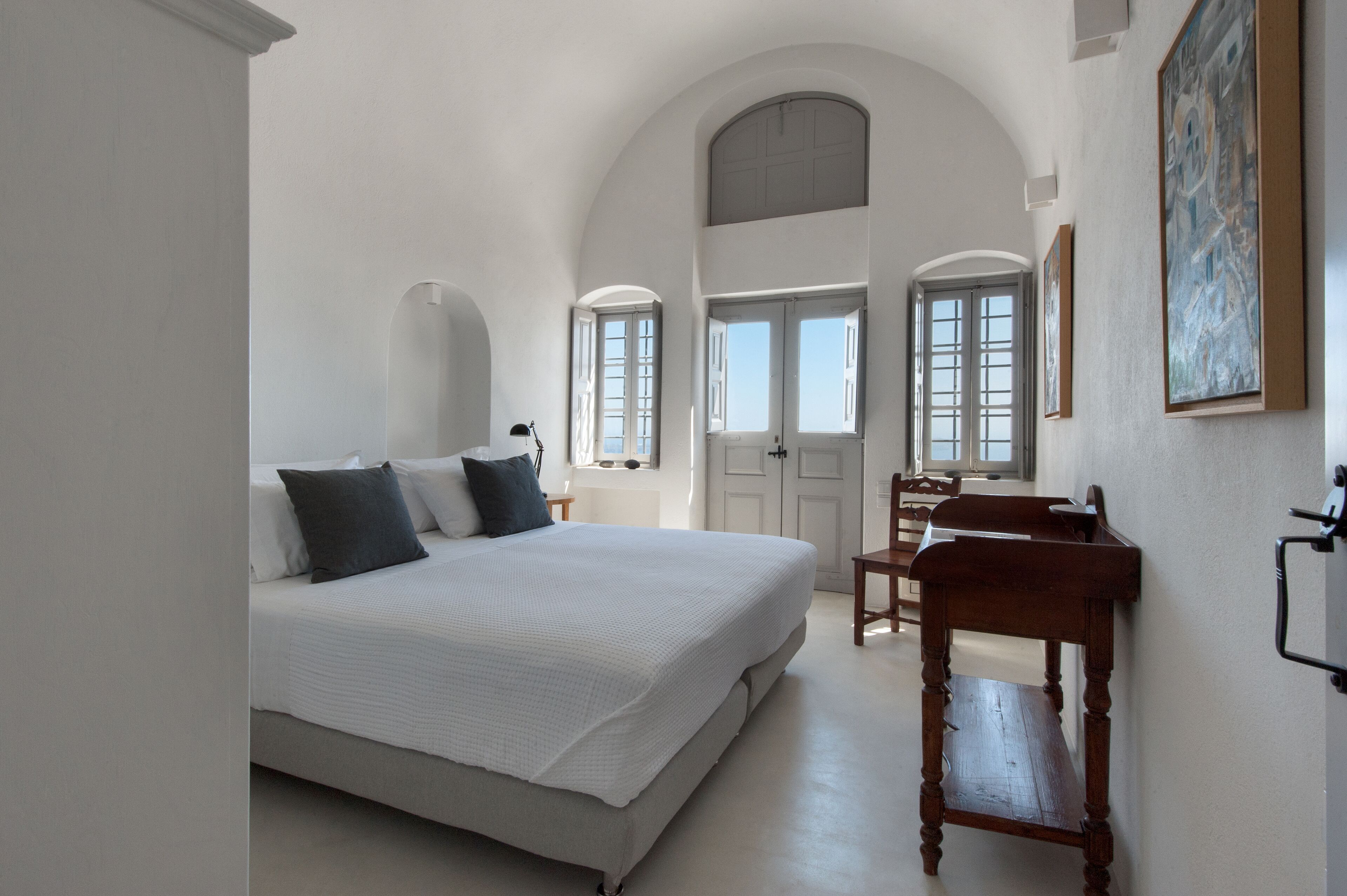 A bedroom with a large bed, two windows, a wooden chair, and a painting on the wall.
