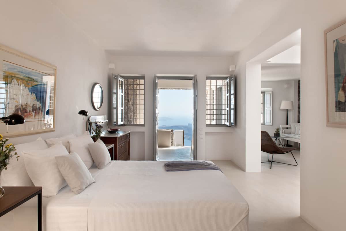Un dormitorio amplio con una cama grande, un escritorio y una silla. Varias ventanas ofrecen vistas al exterior.