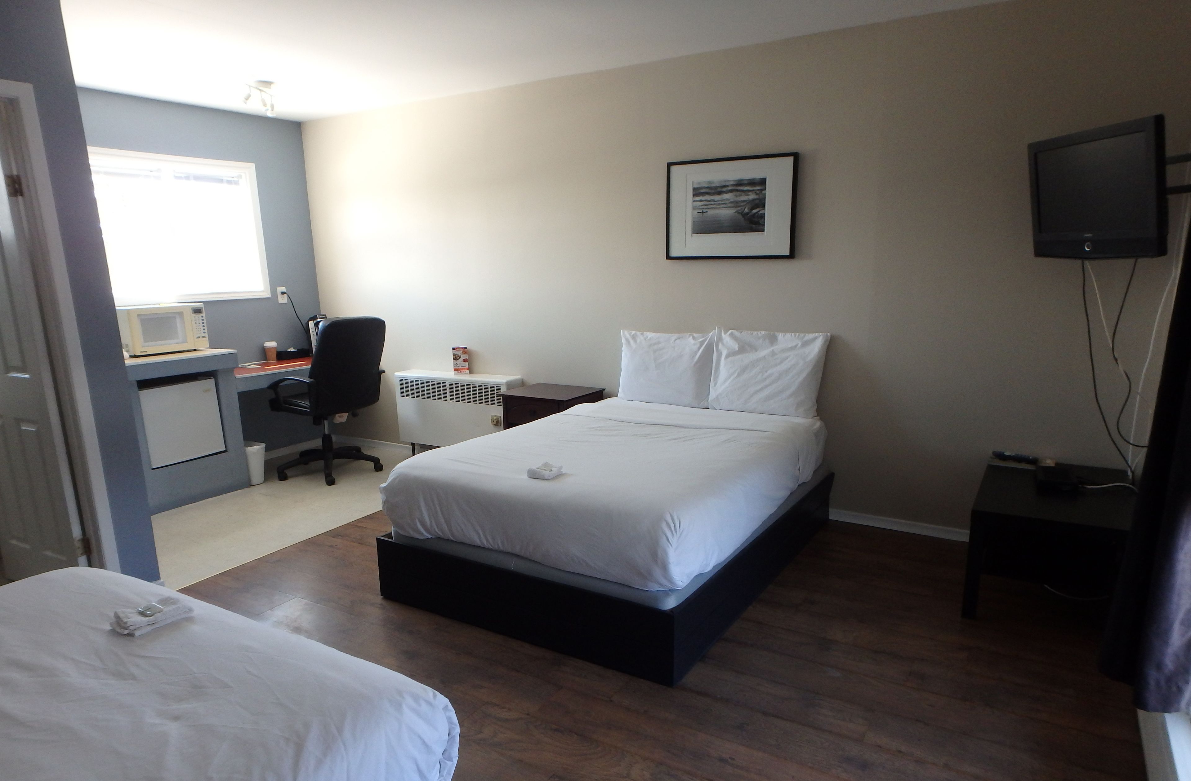 A bedroom with a bed, a desk with a computer, a chair, a TV, and a window.