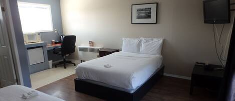 Ein Schlafzimmer mit einem Bett, einem Schreibtisch mit Computer, einem Sessel, einem Fernseher und einem Fenster.