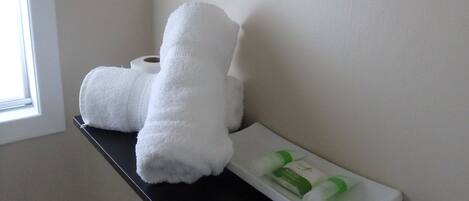 Un baño con un toallero con dos toallas, un estante con toallas enrolladas y artículos de aseo, y un inodoro blanco.