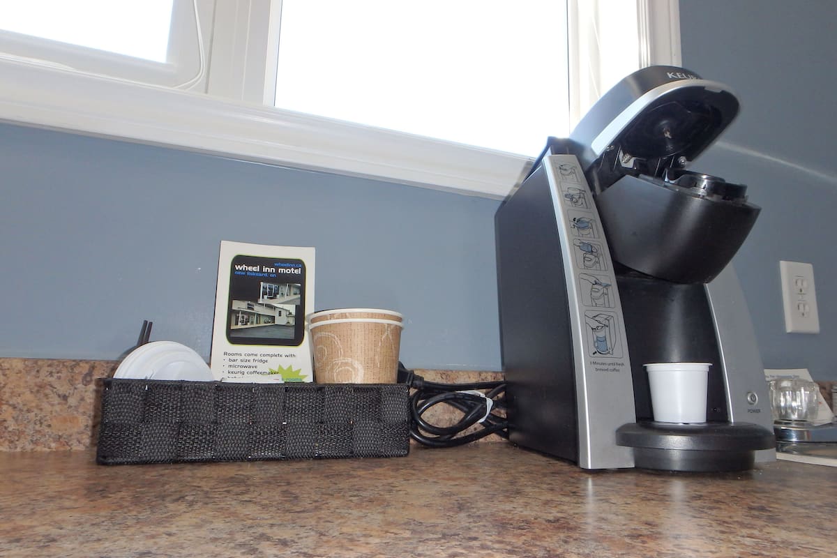 A coffee maker, a basket with a disposable cup, and a brochure on a kitchen counter.