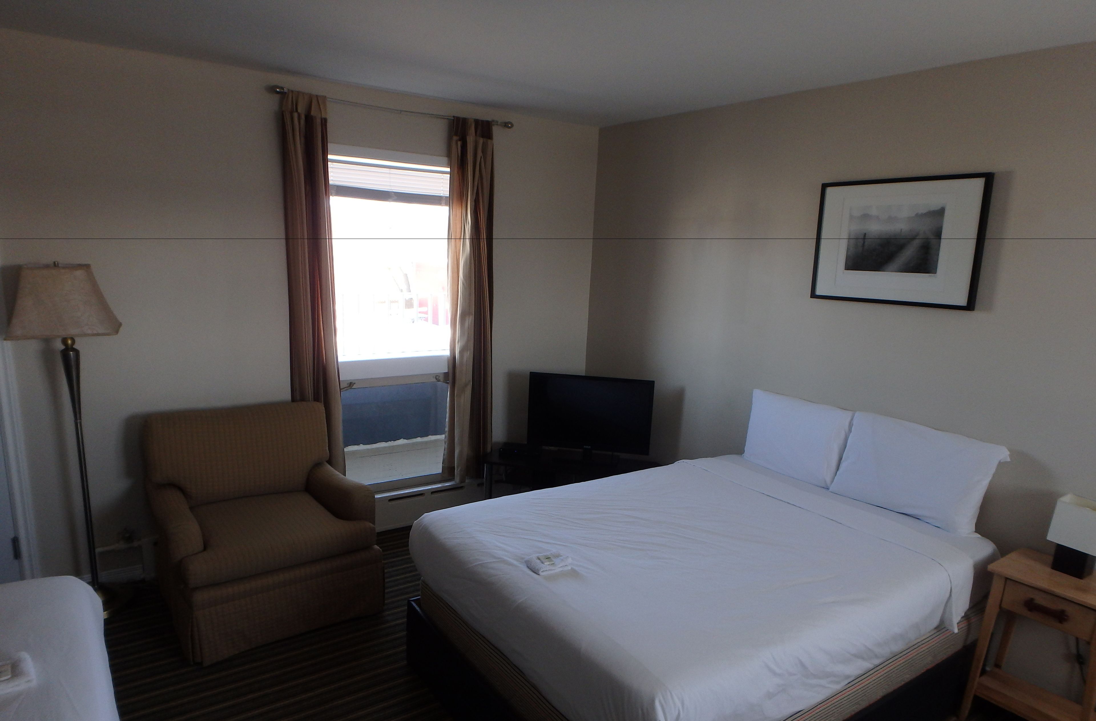 A hotel room with a bed, a chair, a TV, and a window with curtains.