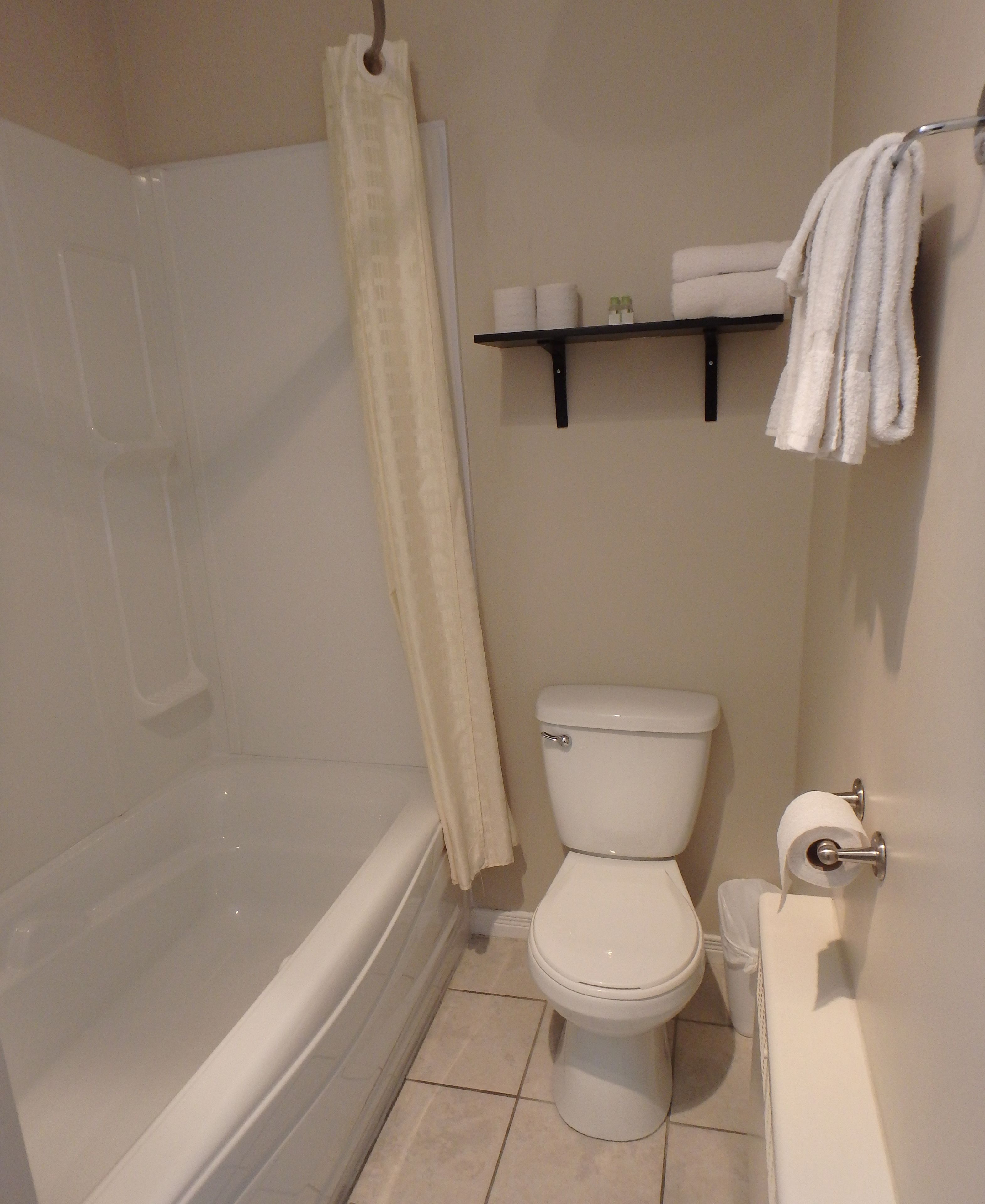 A bathroom with a bathtub, toilet, and a shelf with towels.