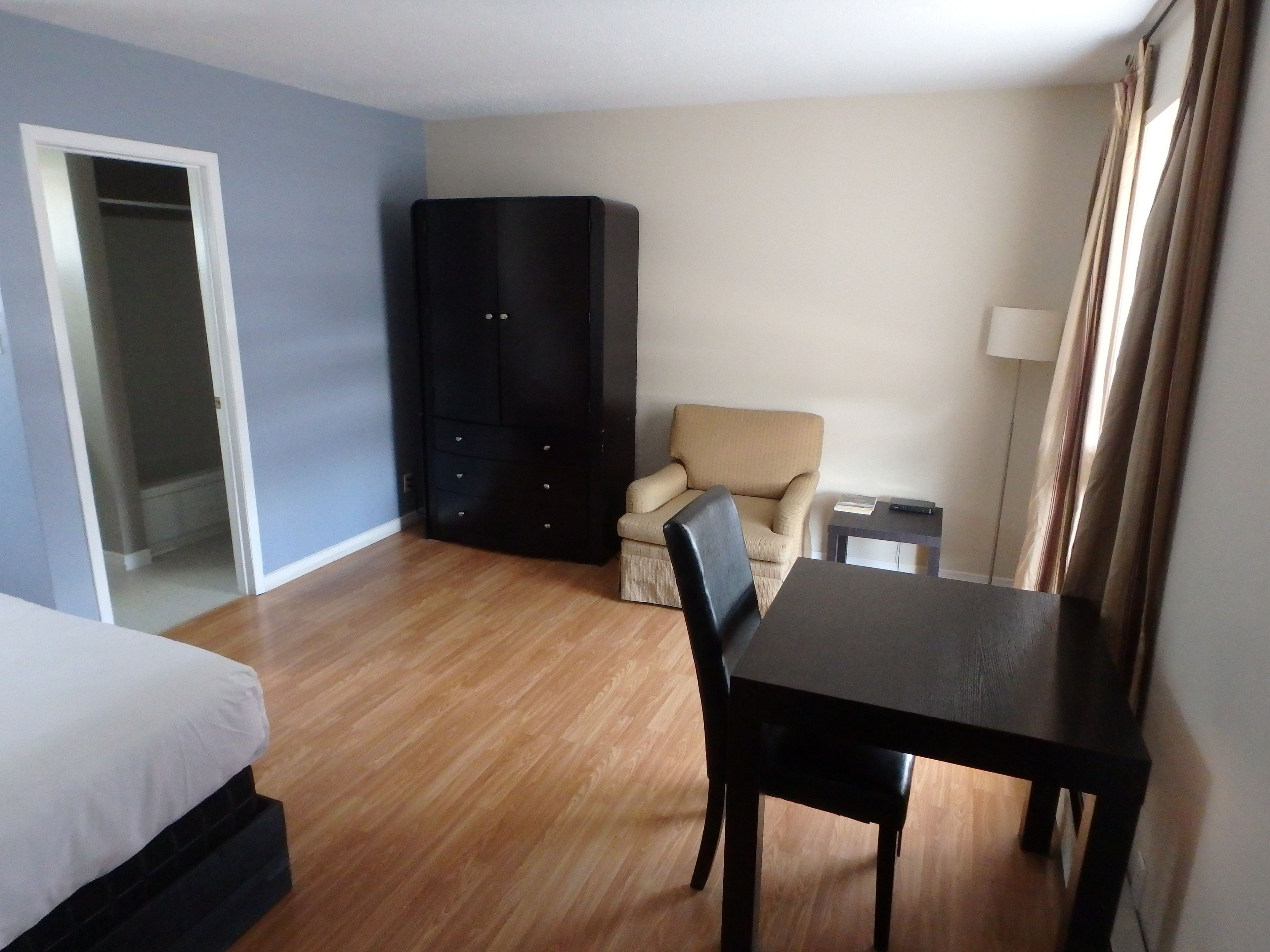 Una habitación de hotel con cama, escritorio, silla, armario y lámpara.
