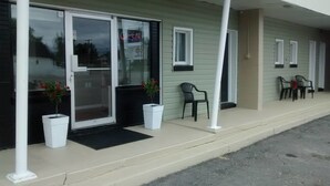 A motel with a covered entrance, two potted plants, and a row of chairs outside. - Wheel Inn Motel (Temiskaming Shores)