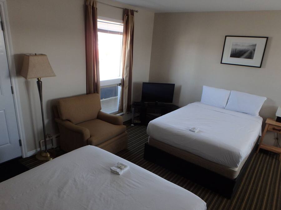 Ein Hotelzimmer mit zwei Betten, einem Sessel, einem Fernseher und einem Fenster mit Vorhängen.