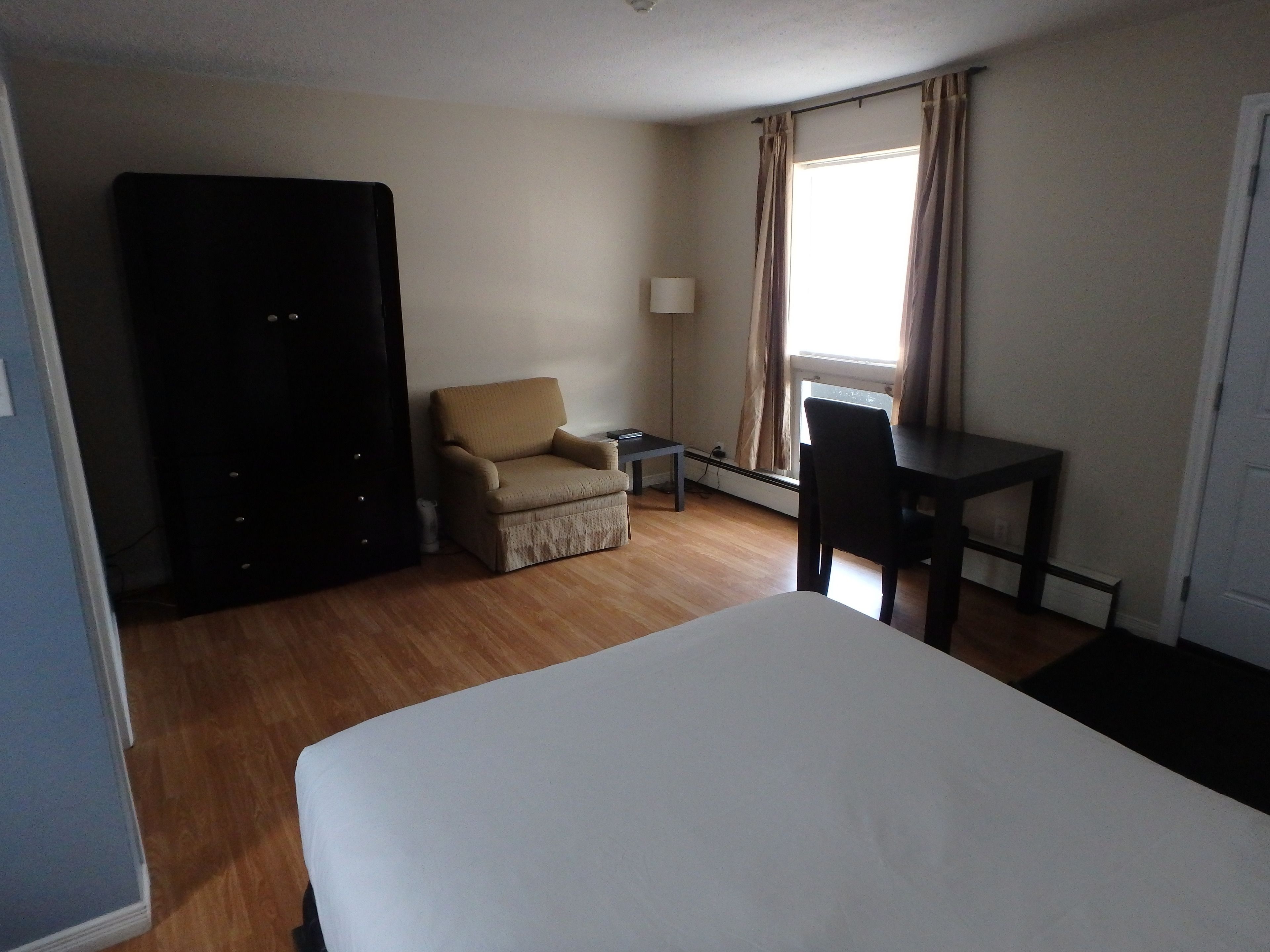 A hotel room with a bed, a chair, a desk, and a wardrobe.