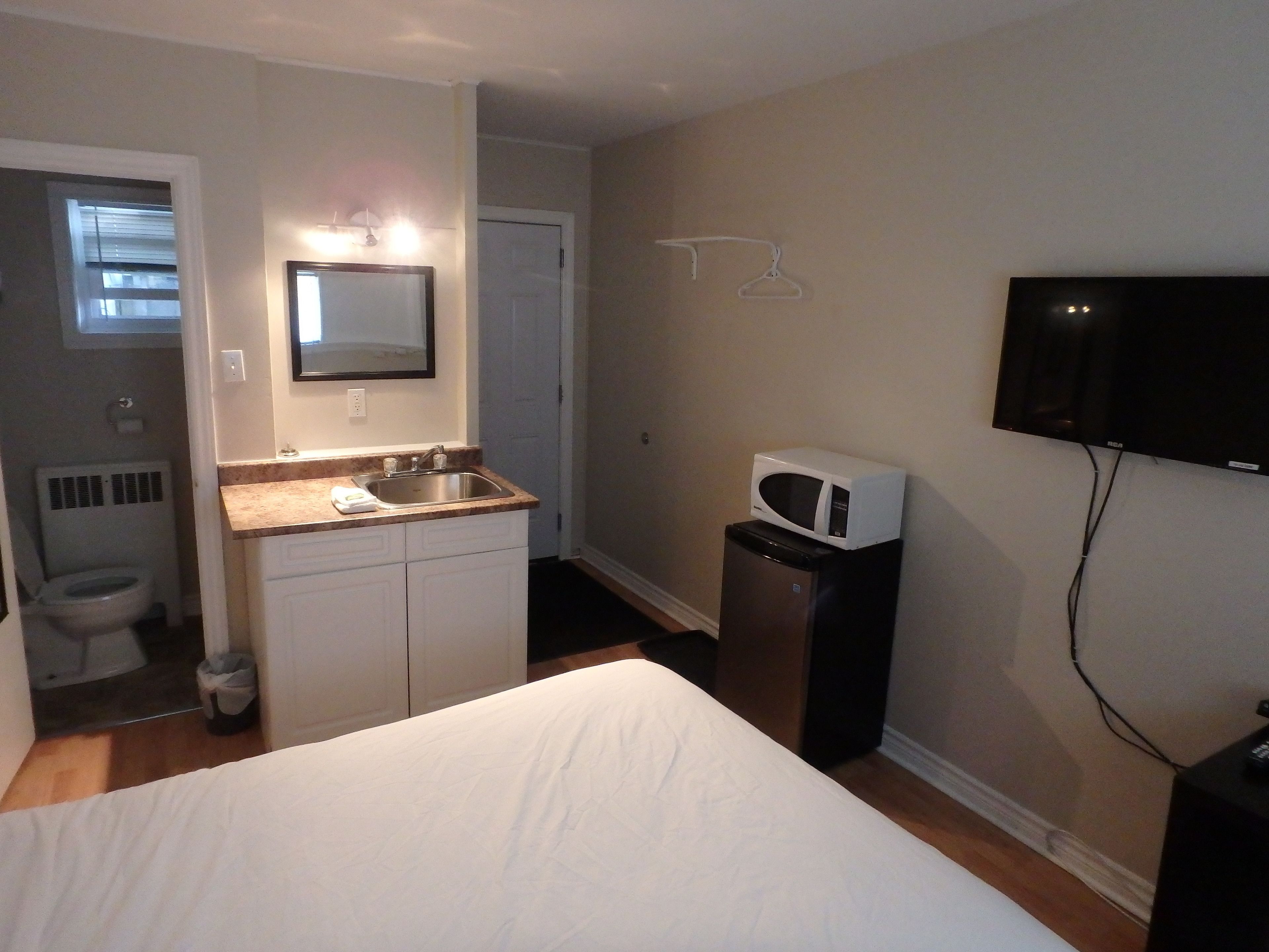 Una habitación de hotel pequeña con una cama, un lavamanos, un microondas, un televisor y una puerta que da al baño.