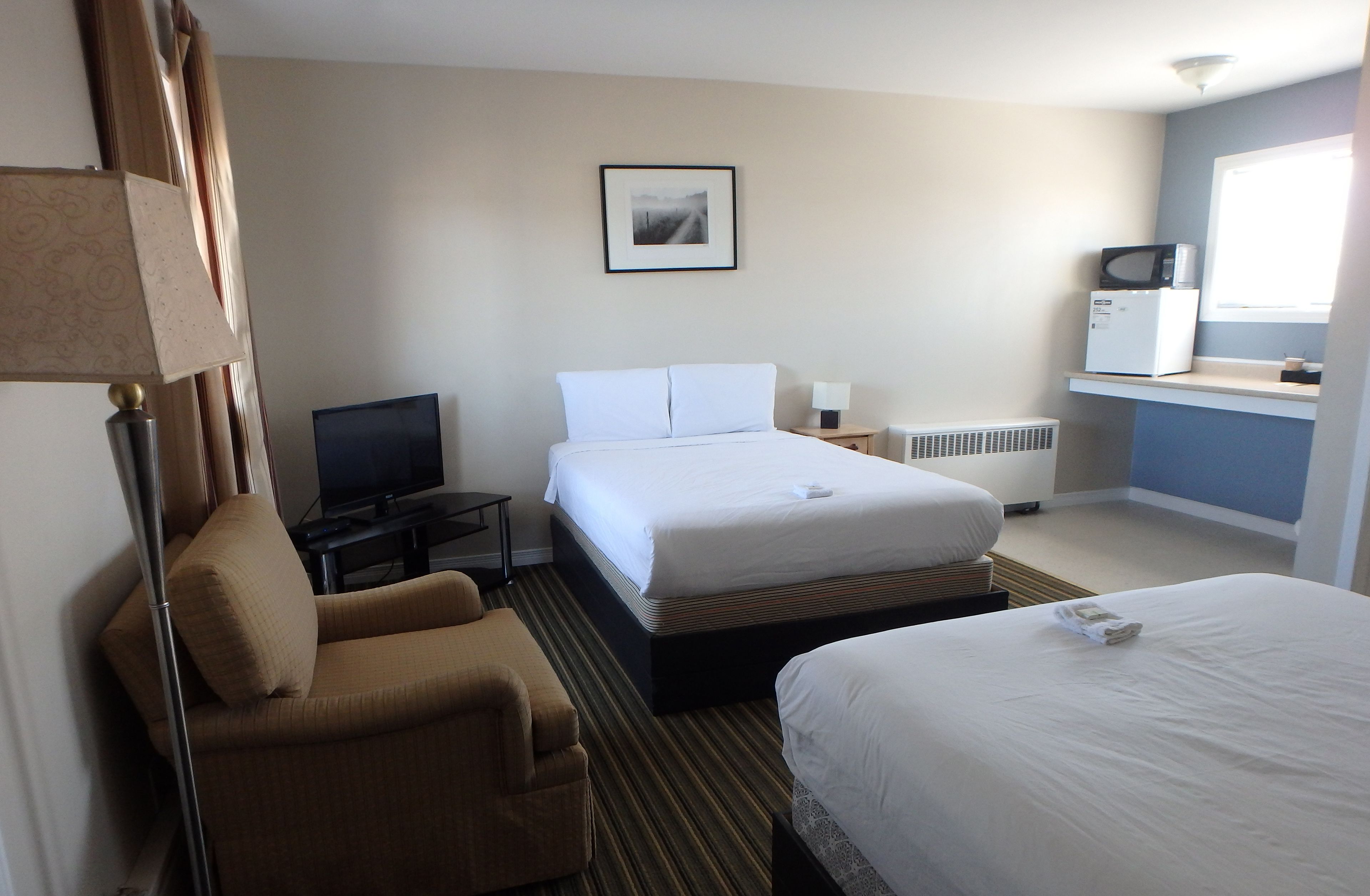 A hotel room with a bed, a chair, a television, a picture on the wall, a microwave, and a window.